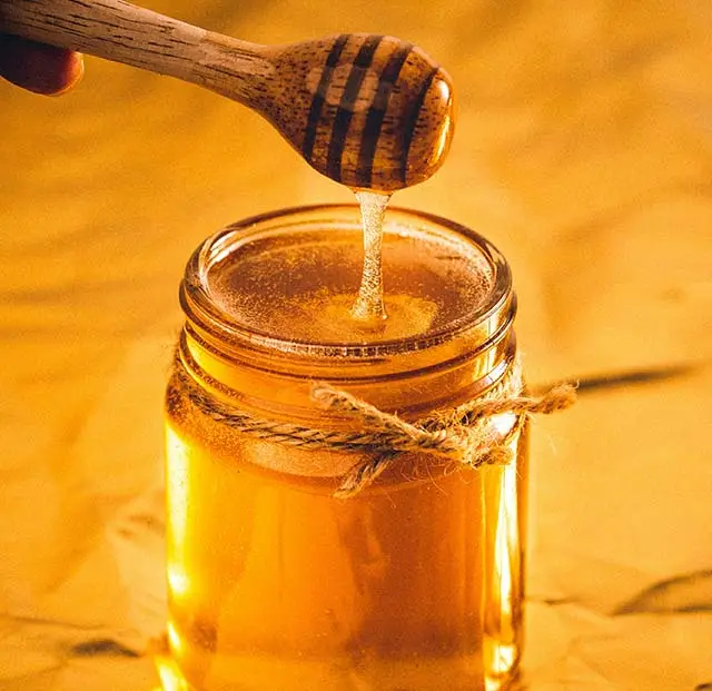honey drizzling from a dipper into a jar